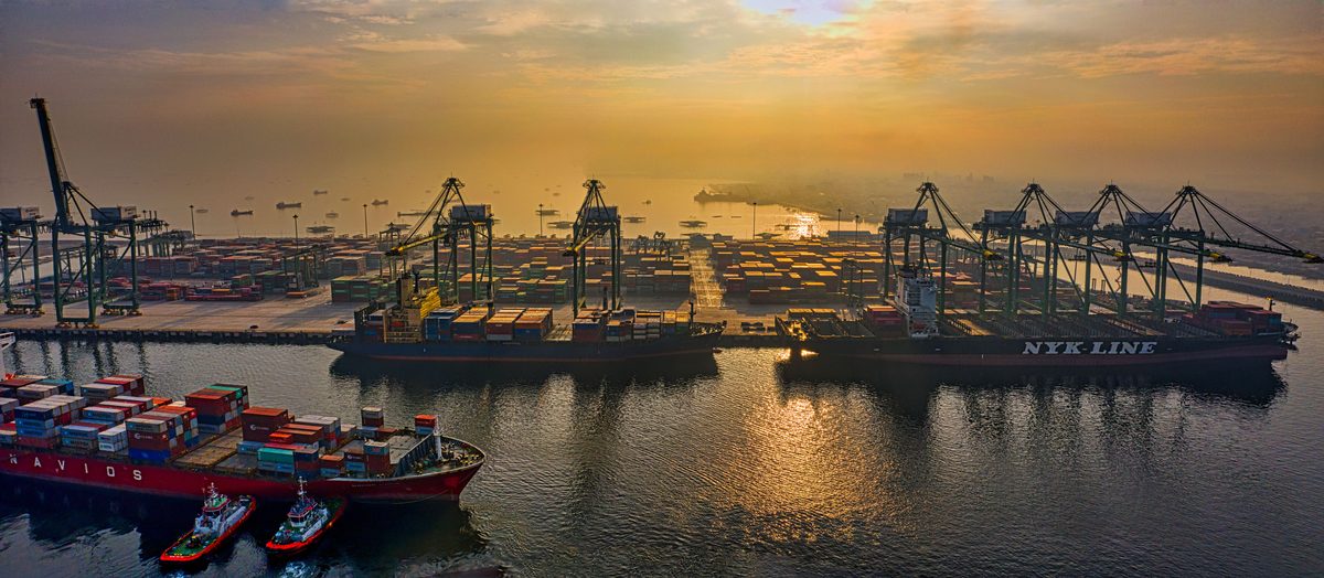 Veduta aerea di un terminal container al tramonto, con navi portacontainer sotto le gru di banchina.